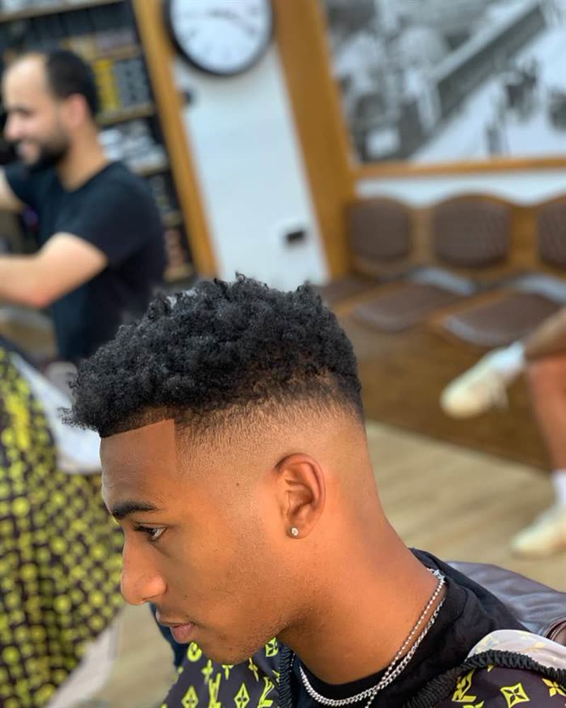 Curly top with a skin fade, barber smiling in the background